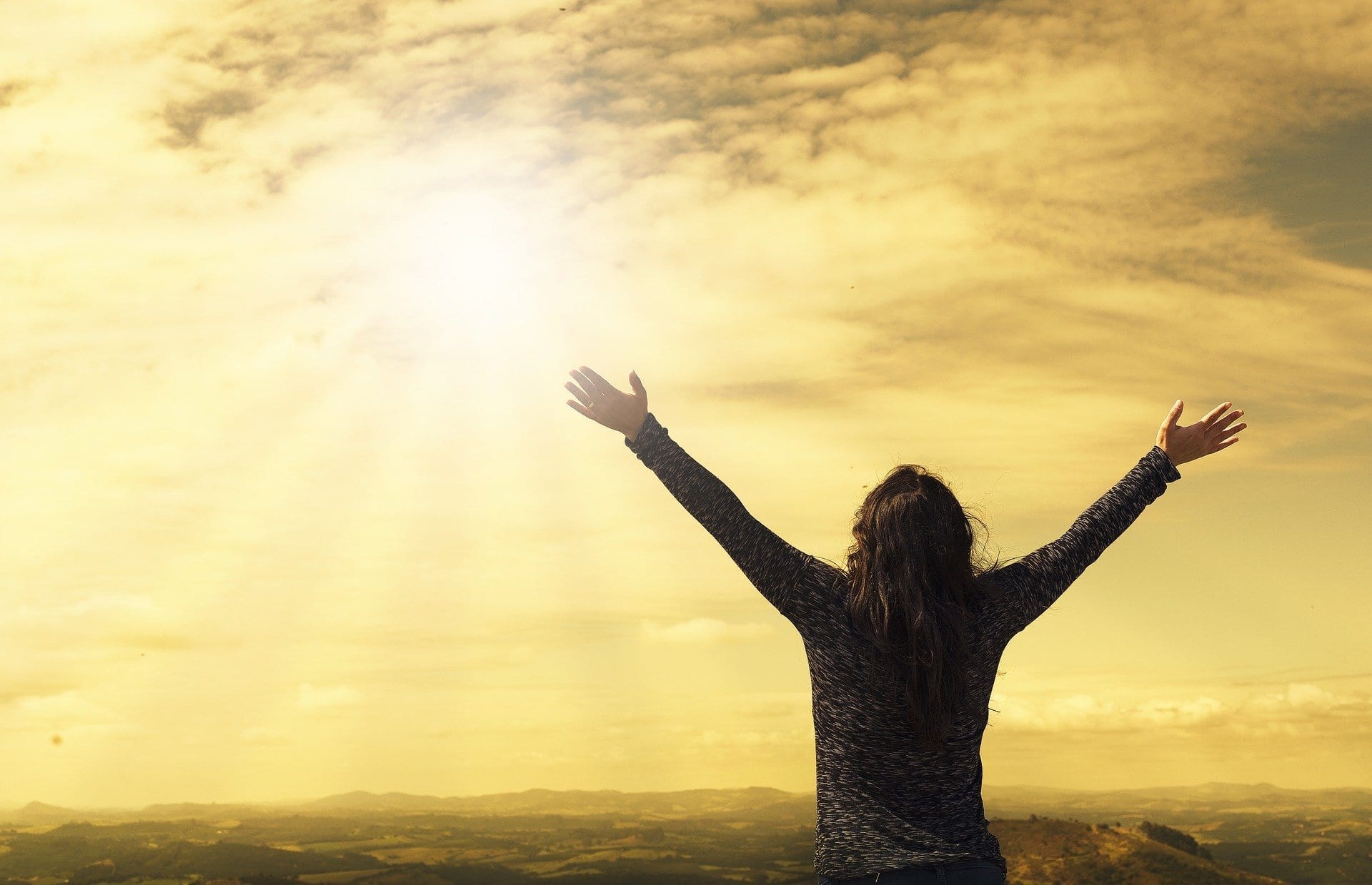 Person with raised arms toward sunset